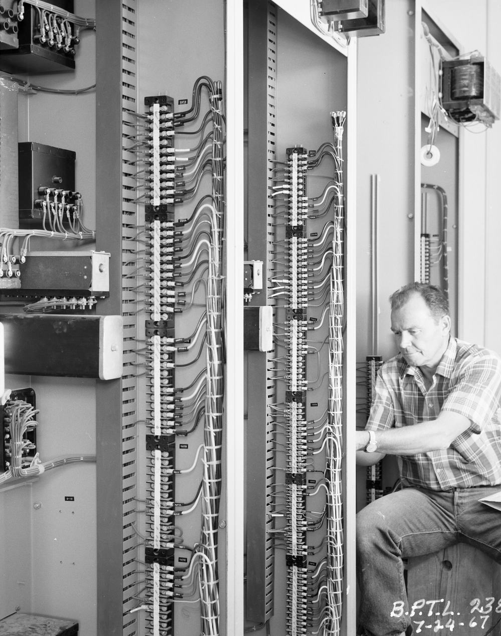 Zwart-witfoto uit 1967 van een man die zit te werken tussen lange rijen klemmen in een schakelkast